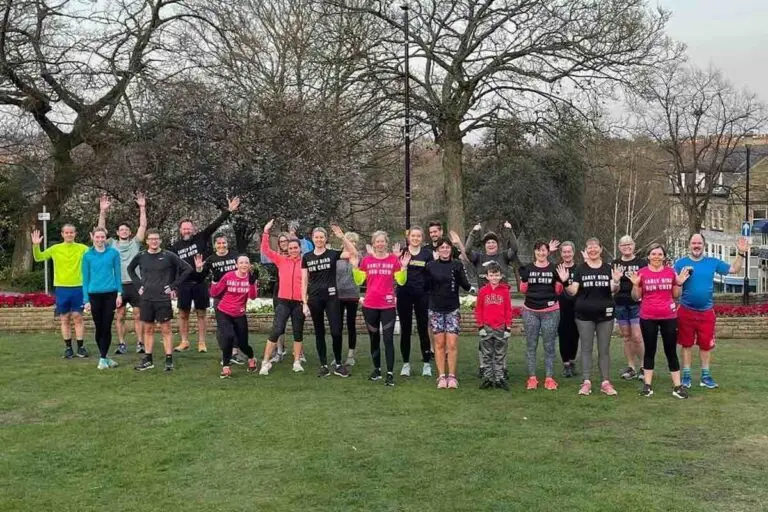 A group from Early Bird Running Crew wave at the camera in a park