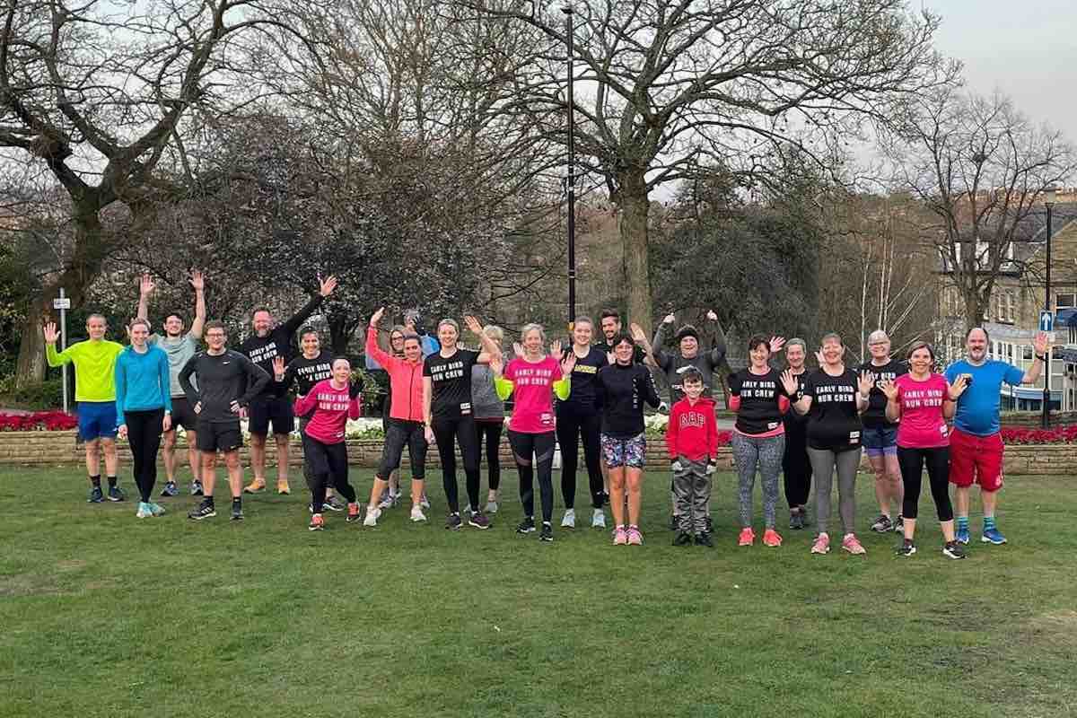 A group from Early Bird Running Crew wave at the camera in a park